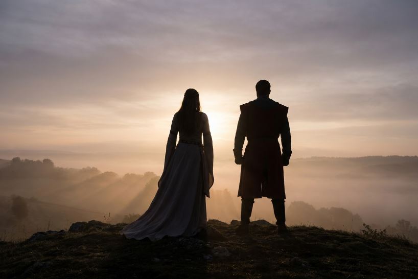 Two figures silhouetted against a foggy sunrise landscape